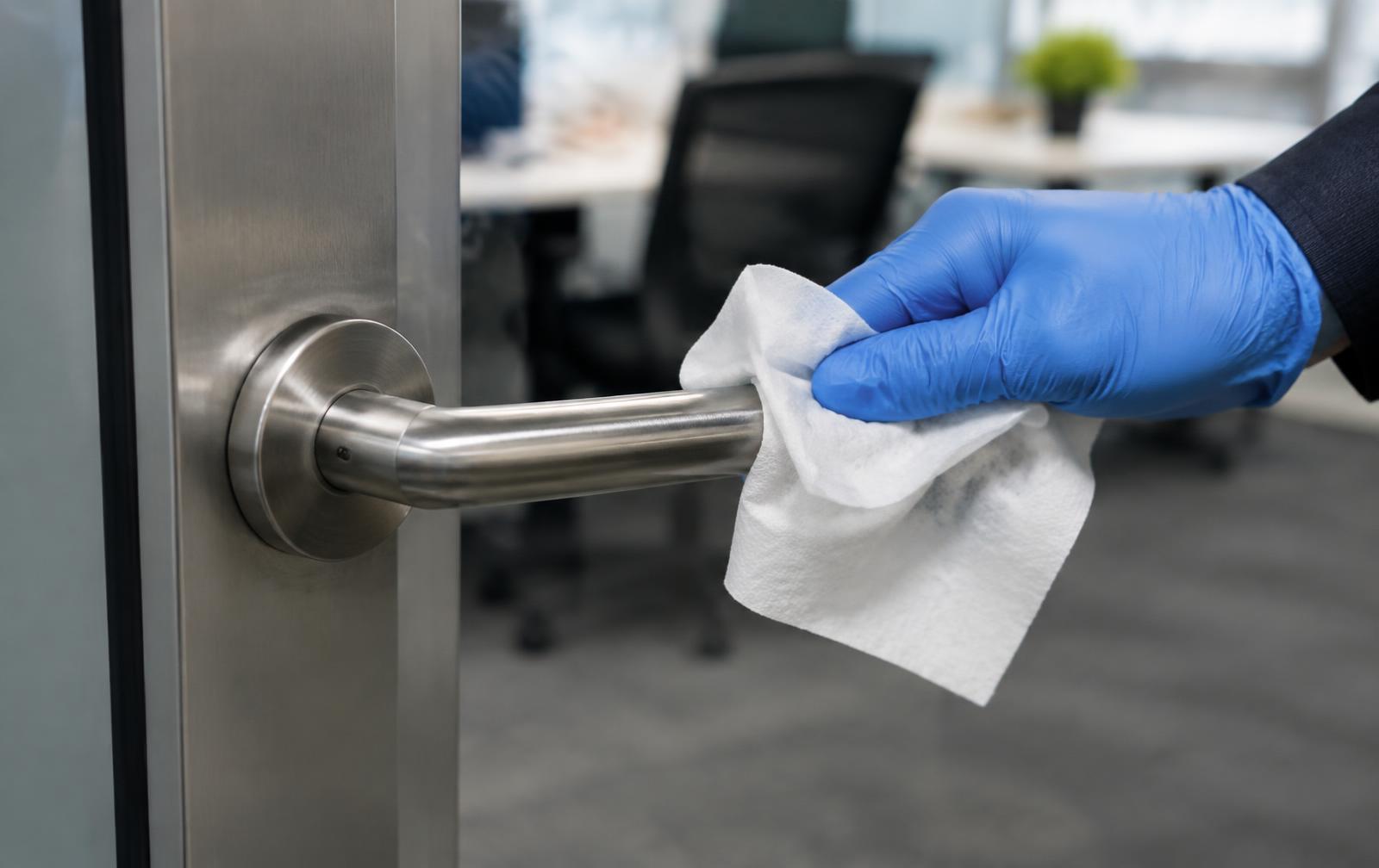 Gloved hand wiping a door handle with a disinfectant cloth